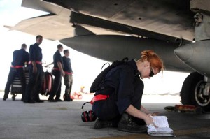 Airman 1st Class Jessica Hinves, US Air Force, kneels under an aircraft.